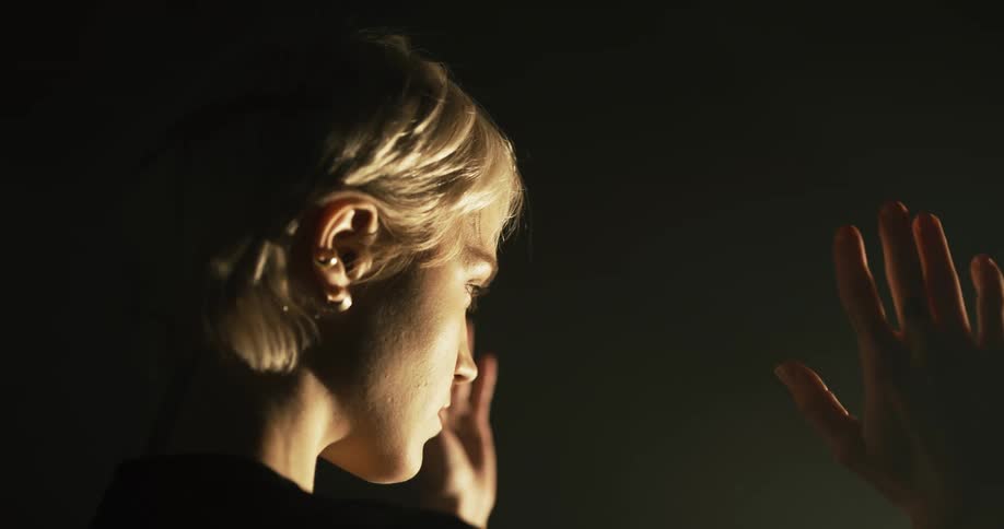 A blonde woman moves her hands in front of her against light