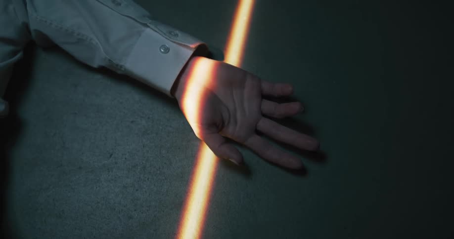 Light shining through narrow opening crosses up turned palm of person lying on floor