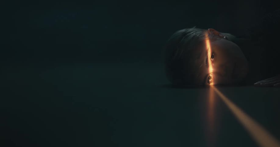 A woman laying on a floor while a ray of light hits her face