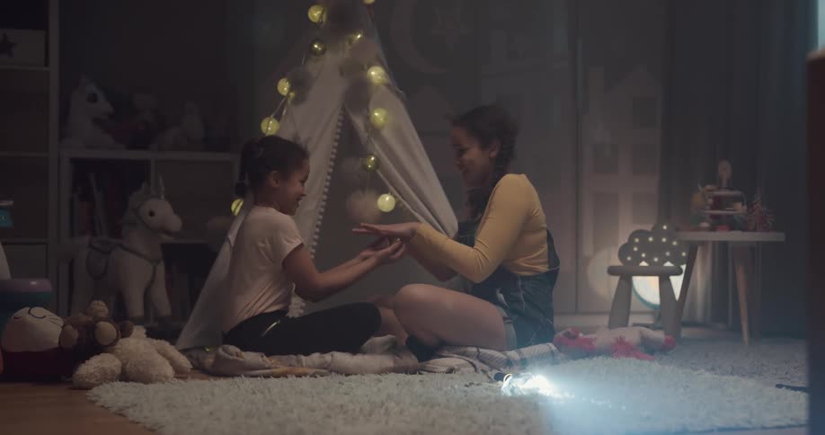 A pair of girls play red hands while sitting on the floor in a childs room in a house
