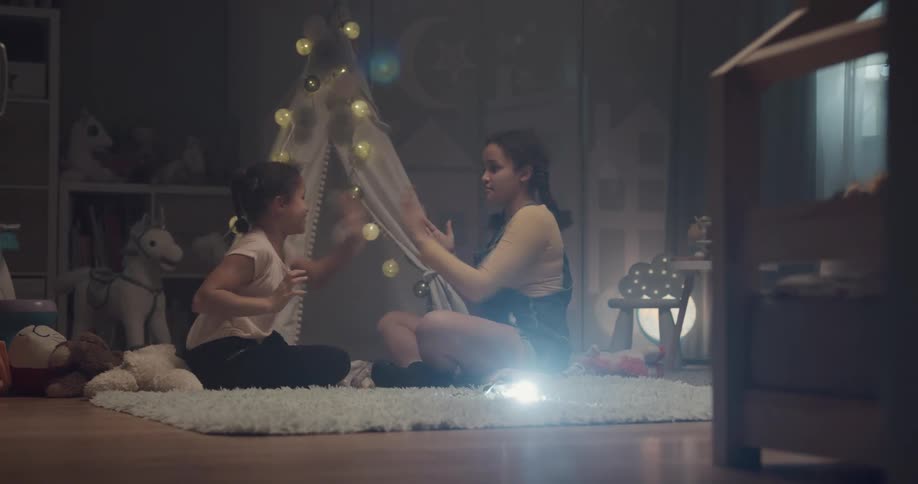 Two young girl playing handclapping games over a rug in a room