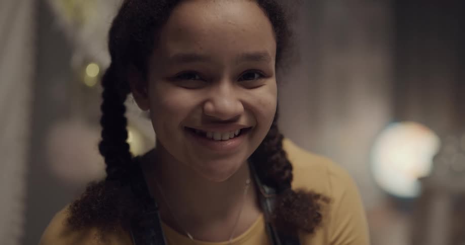 Young girl with pigtails looking at the camera smiling in a room at home