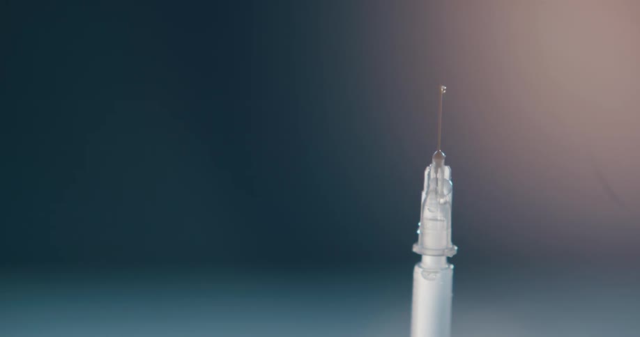 Fingers flick a syringe causing liquid to squirt from the needle