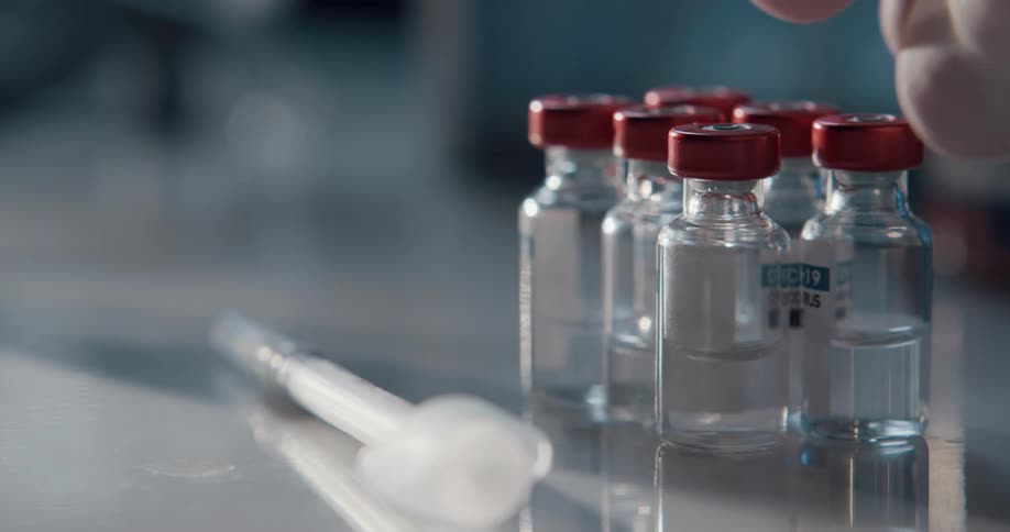 A hand places a syringe next to several bottles and then picks up a bottle
