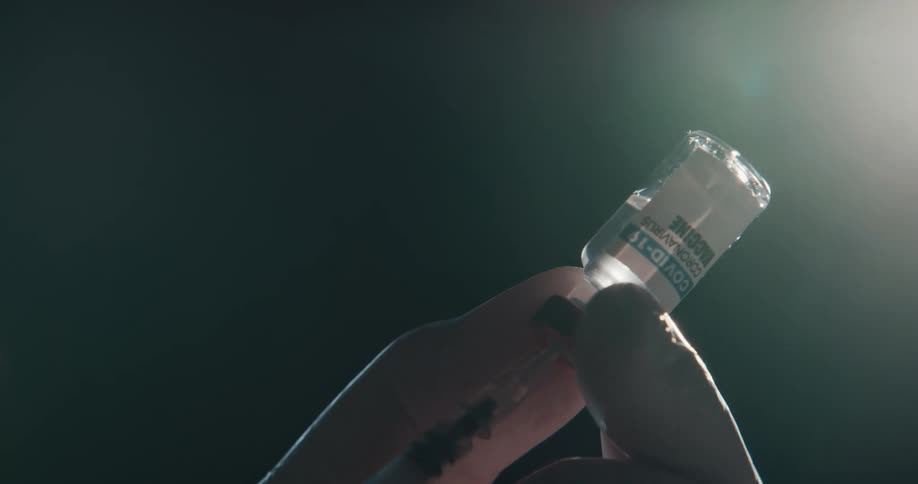 A person uses a needle to extract a portion of covid19 vaccine from a small bottle