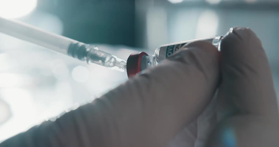 Hand with latex gloves holding a vial being pierced by a syringe