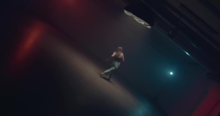 Woman dances in dimly lit room lit by red and blue lights