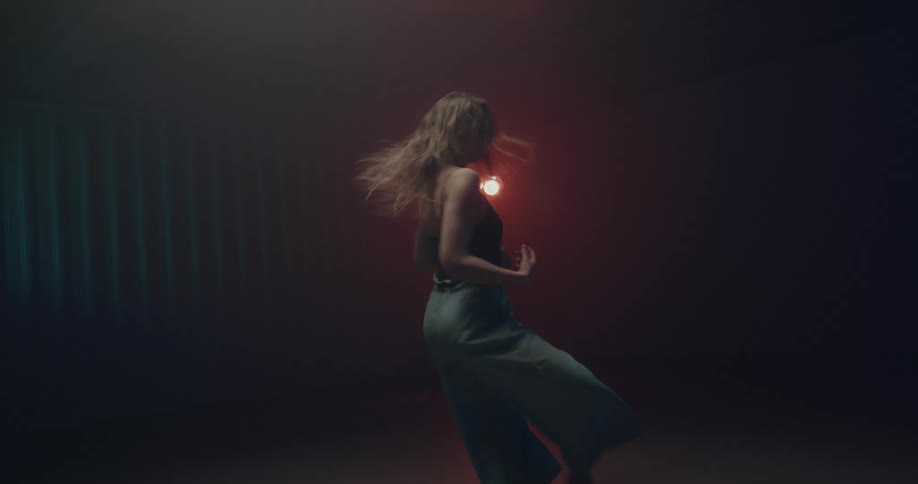 Young woman performing a modern dance on a dimly lit stage with colorful lights