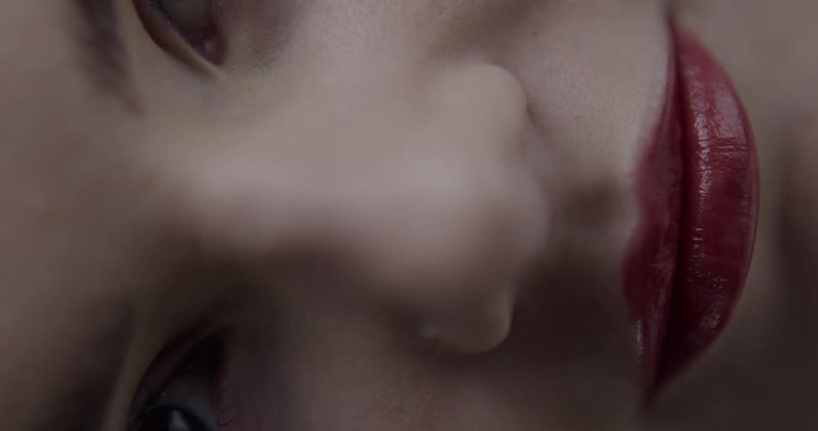 Extreme close up of a young womans face biting her lips covered in bright red lipstick looking at the camera