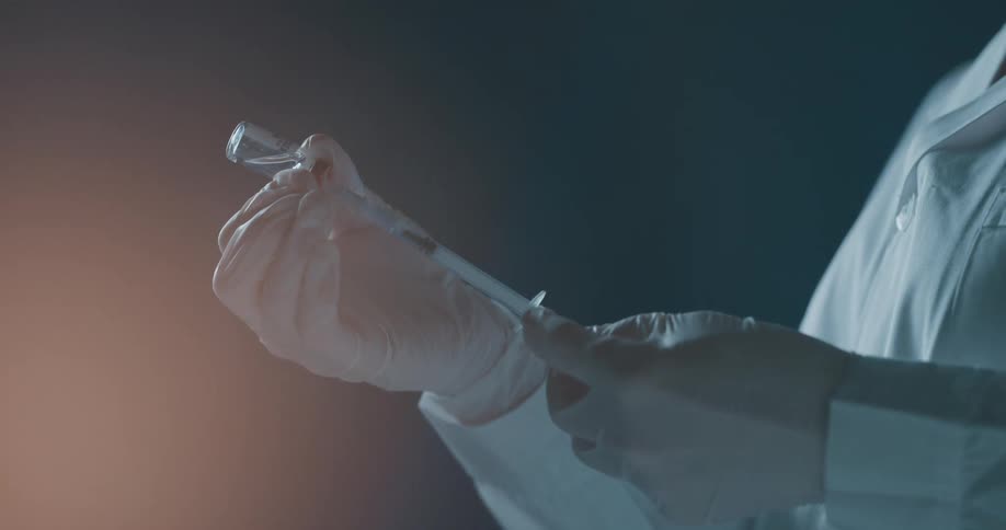 Woman wearing a white lab coat extracts medicine from a small vial with a needle