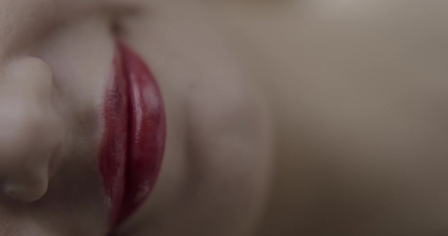 A woman with deep red lipstick smiles subtly before biting her own lip at the camera