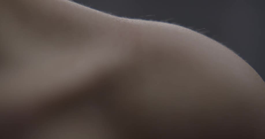A persons shoulder is highlighted while standing topless in a room