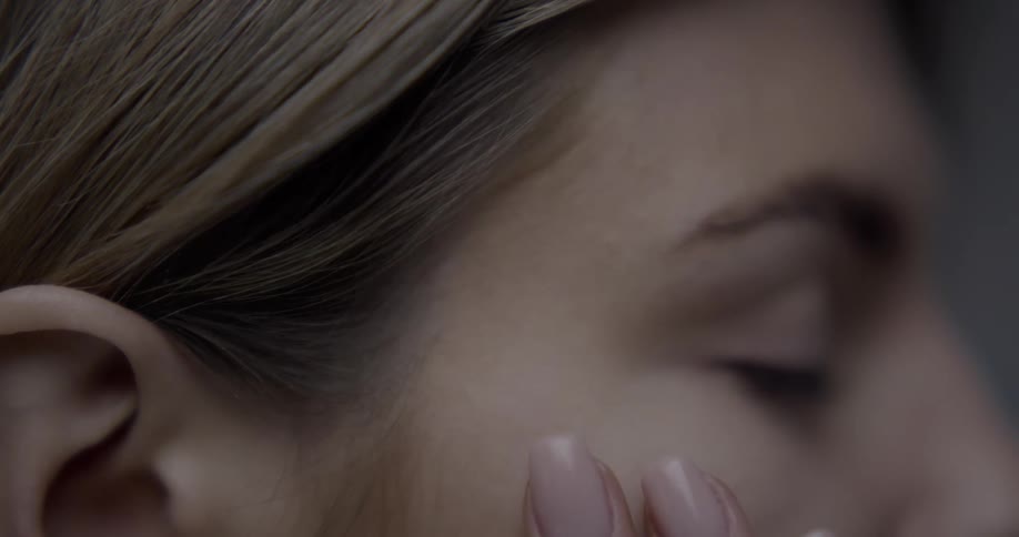 A woman with light brown hair runs her fingers down the side of her face