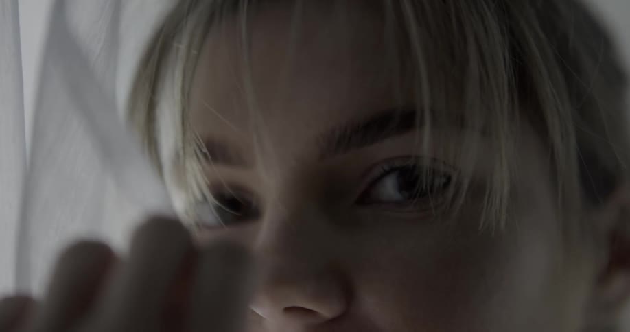 A young woman gently rubs a curtain across her face before looking into the camera