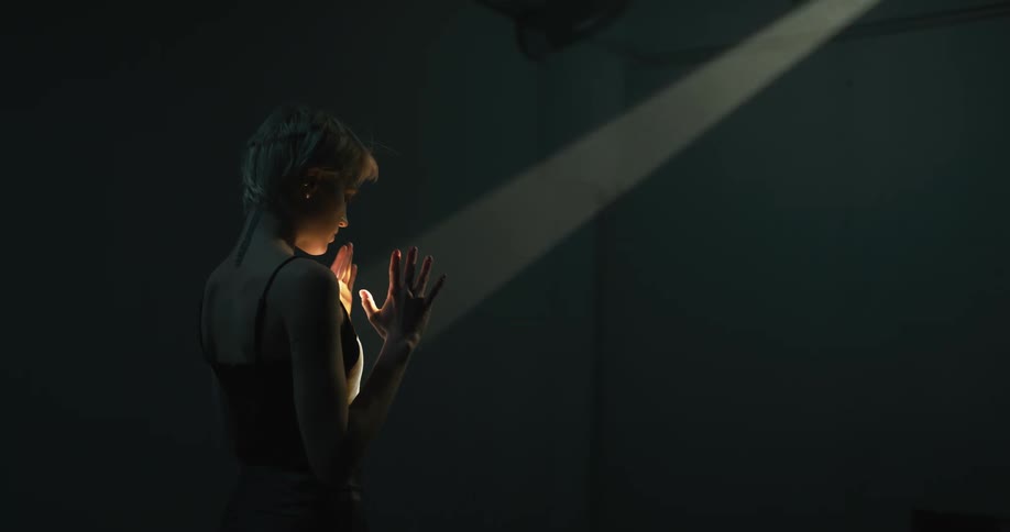 Young short haired blonde woman modeling inside a dimly lit room moving her hands on a spotlight
