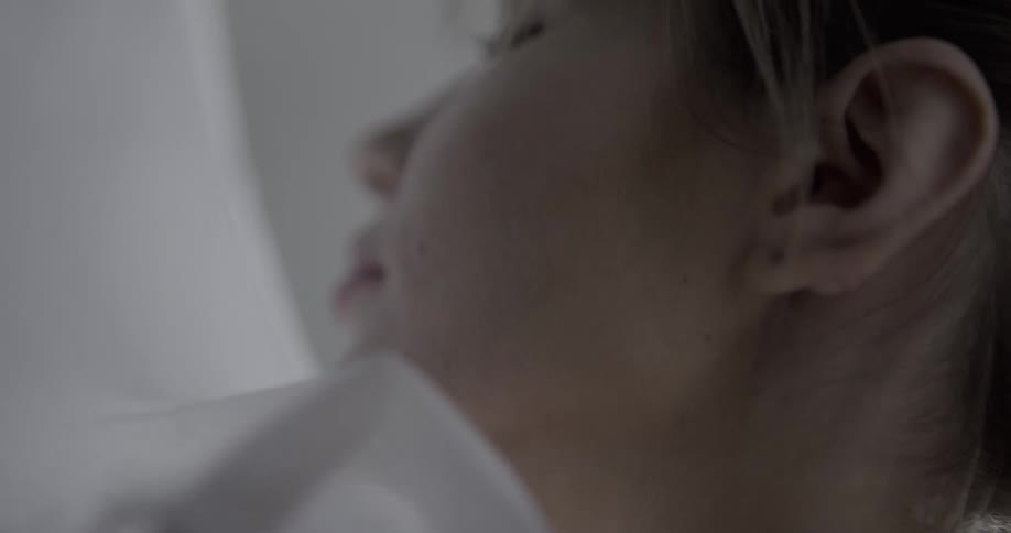 Young woman rubbing gauze veil fabric over her skin in a dimly lit room