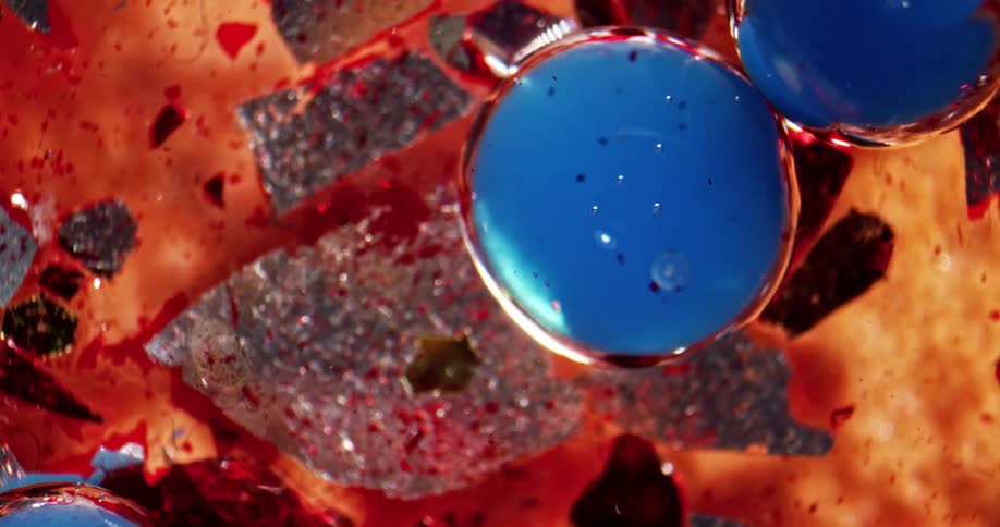 Shards of glass floating on red liquid ink with blue bubbles