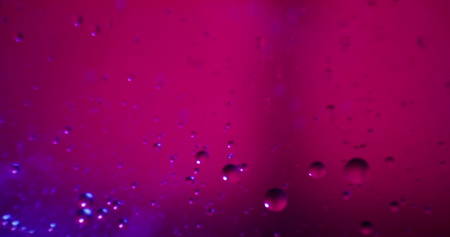A flow liquid that has formed a few bubble with a pink and blue light shinning through