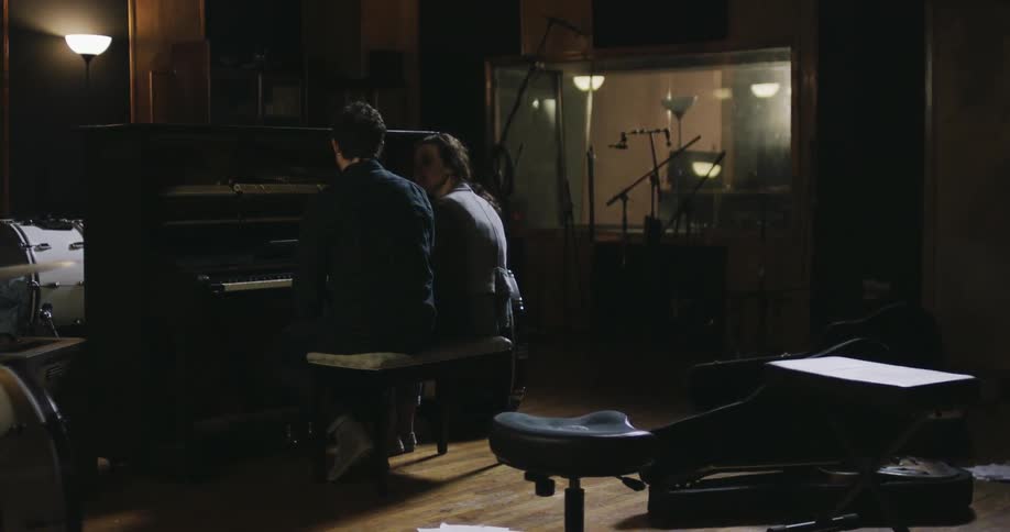 A man and woman sit in front of a piano talking