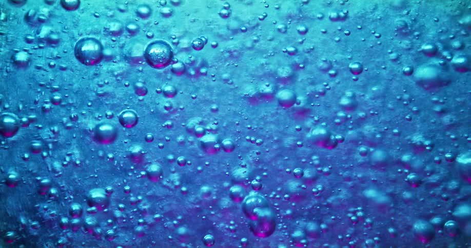 Bubbles move upwards inside of a blue liquid under a microscope