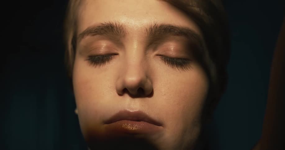 Shadows of hands moving around on the face of a woman who looks up and then closes her eyes