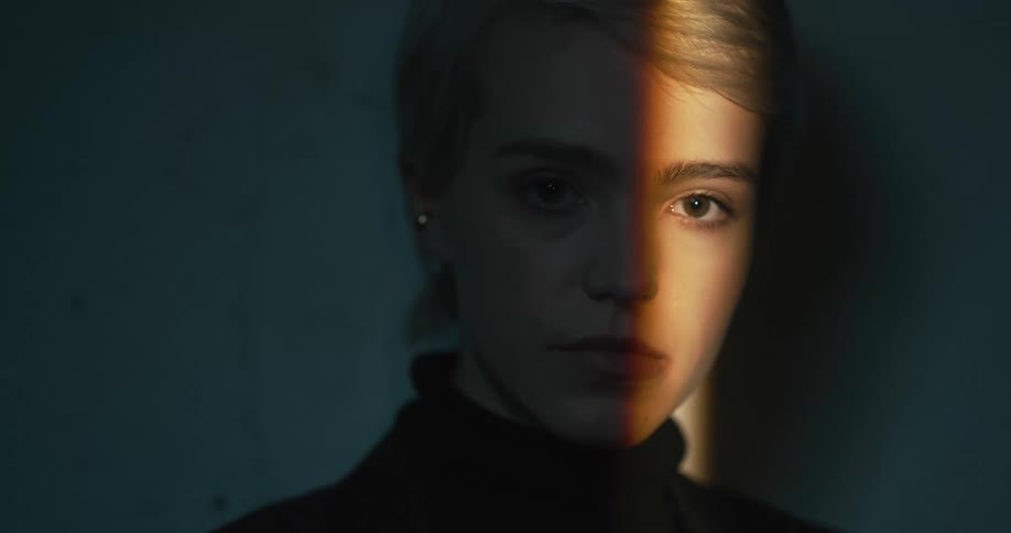 Young blonde short haired woman looks at the camera on a dimly lit room