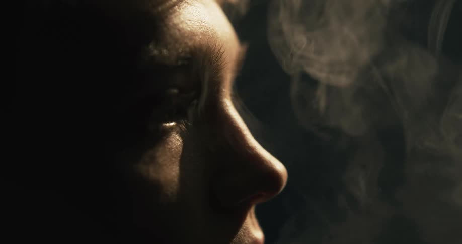 White smoke coming out of a young woman mouth inside a dark room