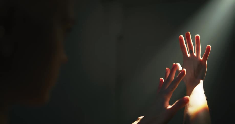 A teenage girl holds her hands up towards the sunlight and looks at them