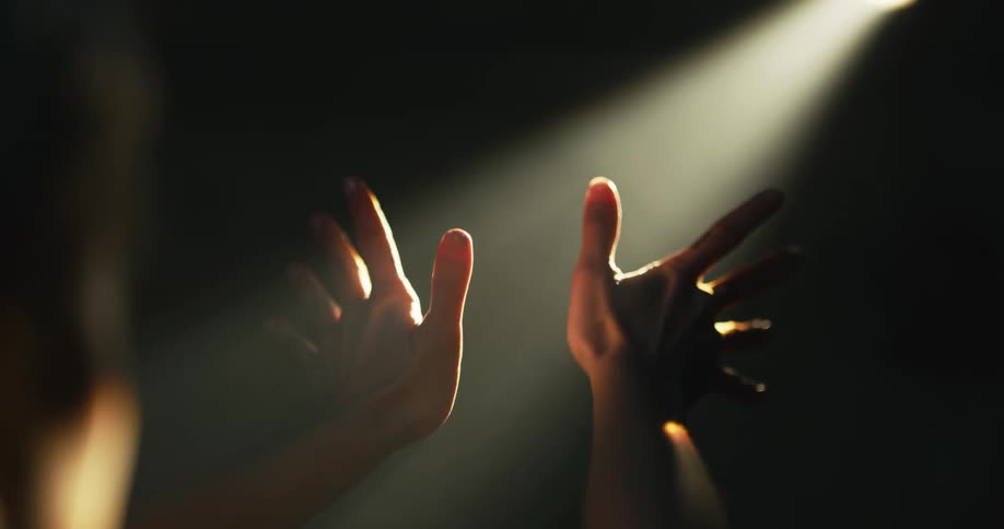 A woman puts her hands up to a beam of light casting down onto her face