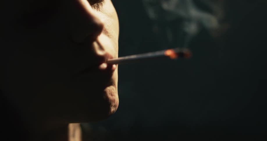 White man smoking a cigarette in a dark room