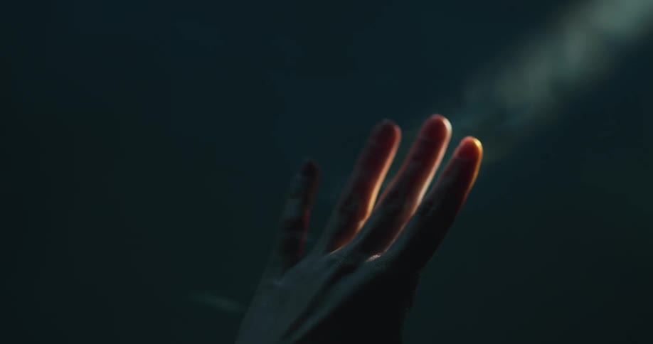 A person holds her hand up in the sun as smoke floats in the air