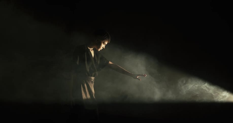 White woman performing in front of a light at a dark room filled with smoke