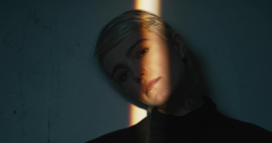A woman leans against a wall and a sunbeam crosses her face