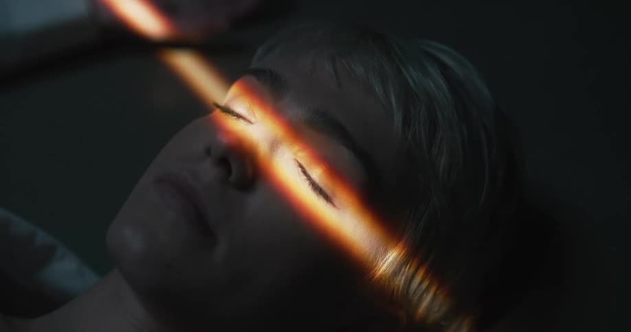 A beam of sunlight streams across a sleeping womans eyes and she then opens her eyes