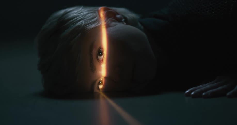 Narrow beam of light shines across eyes of woman lying on the floor in a dark room
