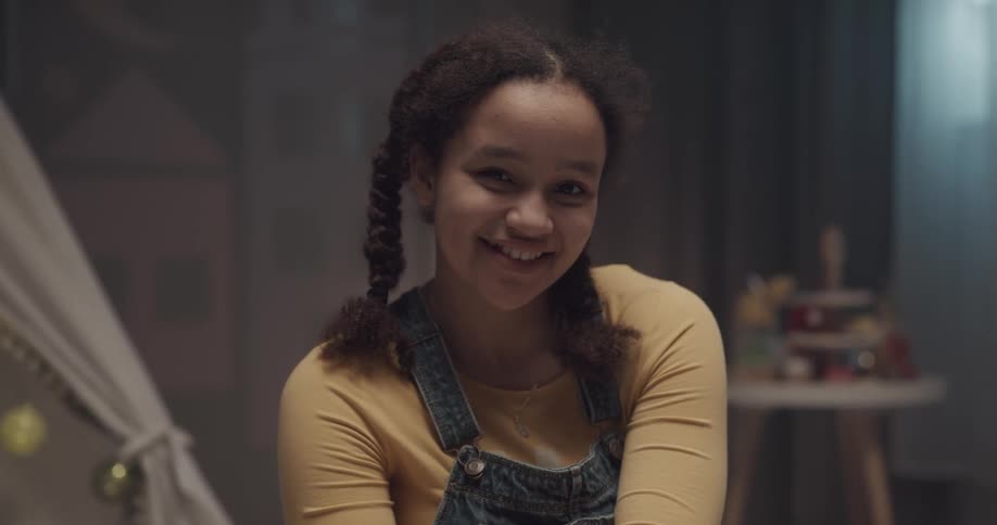 Pretty young black girl sitting indoors smiling at the camera