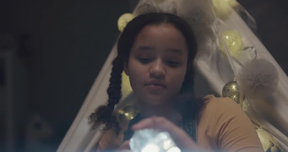 A teenage girl shines a flashlight at a crystal at home
