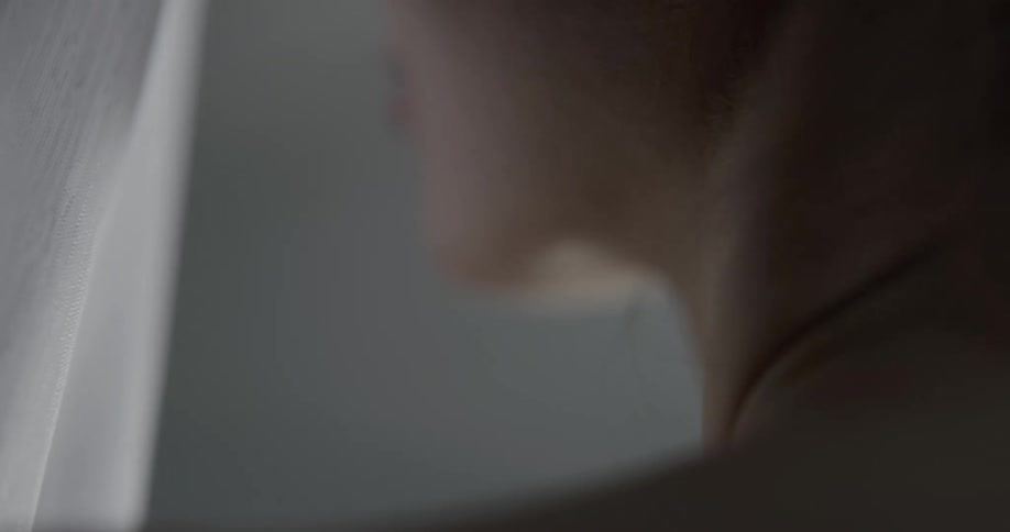 A woman in profile with bare shoulders and neck touching a white piece of fabric