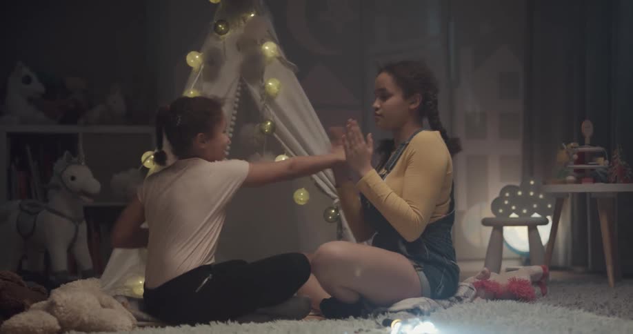 Two sisters slapping hands while playing on the floor of a bedroom