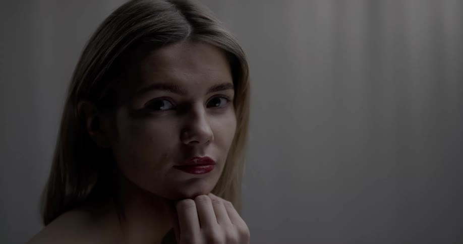 A naked woman sitting contemplatively in an empty room turns to gaze into the camera
