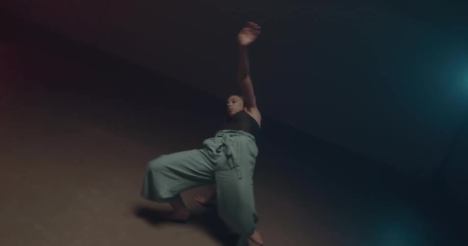 Woman with blue pants and black top dances in dark room