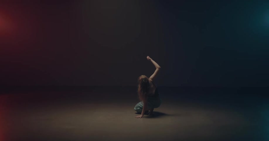 A barefoot young woman dances in a studio illuminated by lighting of three different colors
