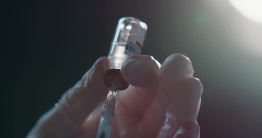 A person poking a needle into a vial
