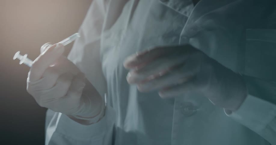 A person wearing white latex gloves opens a syringe package in a dimly lit room