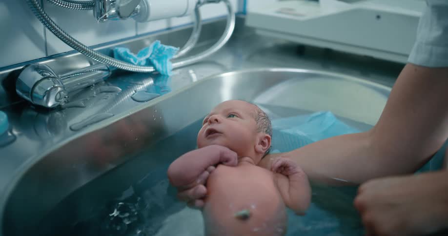 Woman bathes a newborn baby in a stainless steel sink
