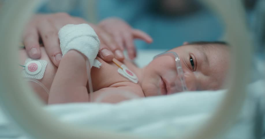 A baby laying on a hospital bed with tubes up his nose with a persons hand on his chest