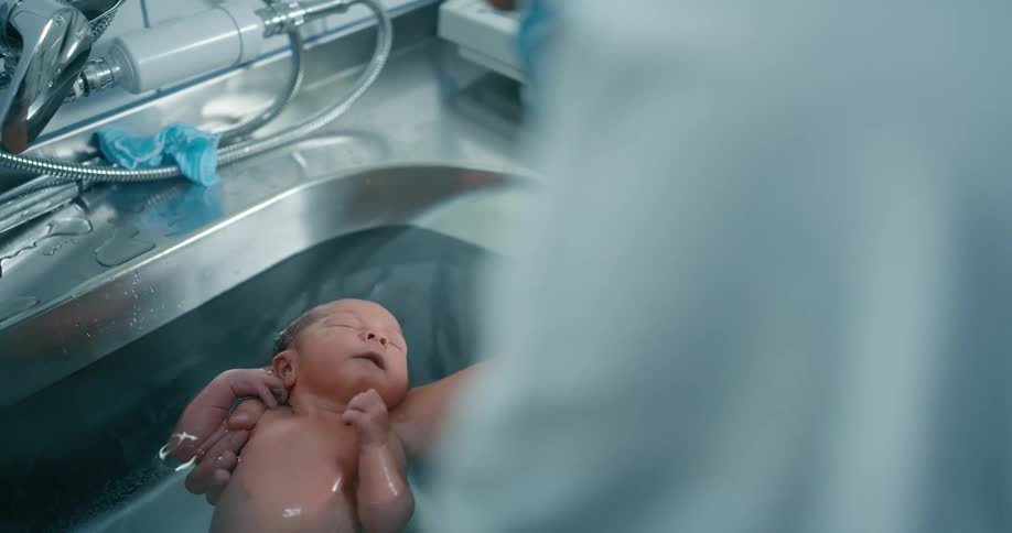 A woman holds a newborn in water in a sink