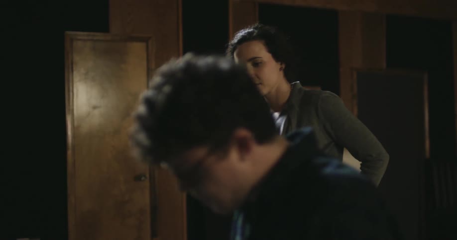 A woman stands and approaches a man paying the piano
