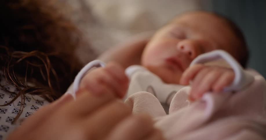 A newborn baby grasps her mothers finger as her mother holds her