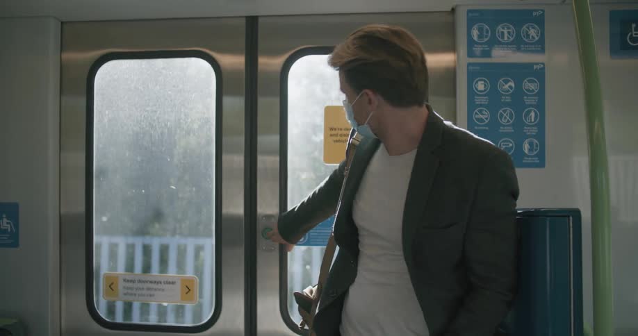 A man riding a subway pushes the button by the door when it stops and gets off